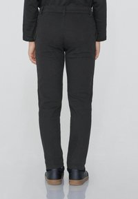 Černé slim-fit kalhoty vyrobené z bavlněné směsi s hladkou texturou. Mají poutka na pásek a zadní kapsy, nošeny s černými teniskami.