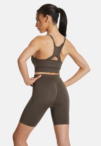 Reggiseno sportivo marrone con design a racerback e dettaglio a taglio, abbinato a pantaloni corti a vita alta coordinati, entrambi realizzati in un tessuto morbido e elastico.