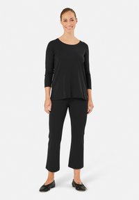 Czarna bluzka z długim rękawem i okrągłym dekoltem w połączeniu z czarnymi spodniami typu dzwony, wykonanymi z gładkiego, elastycznego materiału. Obuwie: czarne baleriny.
