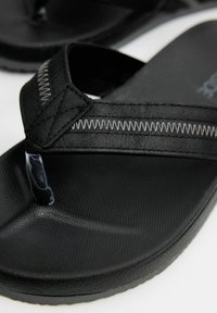 Chanclas negras con suela de goma texturizada, tiras de tela y detalle de costuras en contraste. Diseñadas para uso casual.
