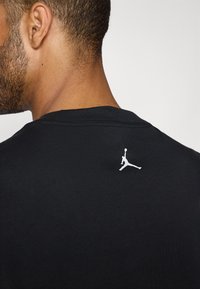 Camiseta negra con un logo de Jordan blanco en el cuello de la espalda. Hecha de una tela suave con un diseño clásico de cuello redondo.