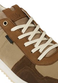 Zapatillas en tonos marrón y tostado, con materiales de malla y ante, parte superior texturizada, cordones blancos y una etiqueta de logo en la lengüeta acolchada.