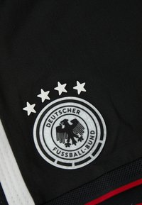 Μαύρη αθλητική φανέλα με κυκλικό έμβλημα που απεικονίζει έναν μαύρο αετό και κείμενο "DEUTSCHER FUSSBALL-BUND", πάνω από τέσσερις λευκούς αστέρες.