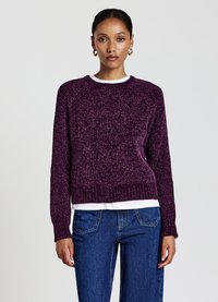 Lila gestrickter Pullover mit strukturiertem Muster, Rundhalsausschnitt und gerippten Bündchen. Über einem weißen Hemd getragen, kombiniert mit blauen Jeans.