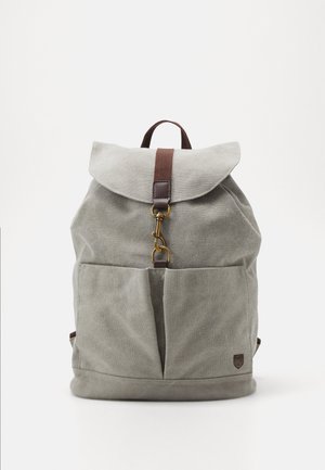 Grau canvas Rucksack mit einem Deckel, braunem Riemen und goldfarbenen Beschlägen. Verfügt über Vordertaschen und eine strukturierte Oberfläche.