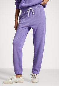 Lila bomullssweatpants med elastisk midja och vit dragsko. Har en avsmalnande bendesign och mjuk texturerad tyg.