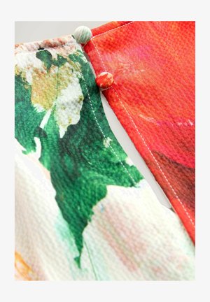Multicolored textile with floral design and contrasting red section. Features green leaves, pink flowers, and decorative fabric buttons.