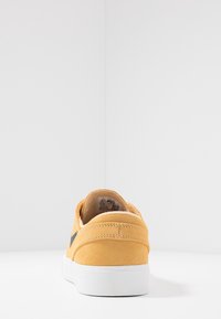 Baskets en suède jaune avec une finition texturée, semelle en caoutchouc blanche et logo noir contrastant. Présente un design minimaliste et des lignes épurées.