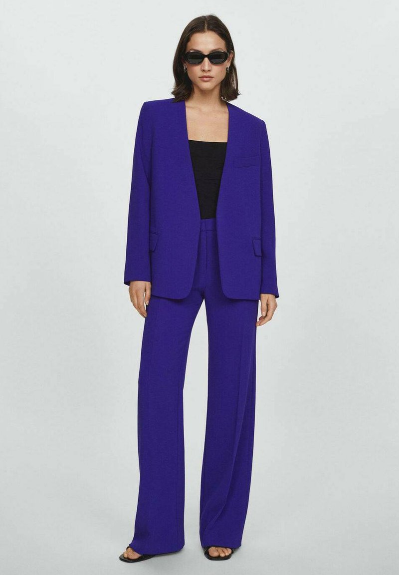 Blazer viola vivace con pantaloni lunghi a gamba larga. Tessuto liscio, design minimalista e dettaglio della tasca sul blazer. Top nero sotto.