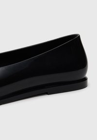 Scarpa piatta nera con una finitura liscia e lucida, forma arrotondata e design minimalista. Presenta un tacco basso e solido e un bordo senza cuciture.