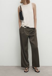 Haut sans manches en maille beige associé à un pantalon large olive, ceinture noire et petit sac à main noir. Le mannequin porte des tongs noires.