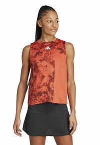 Top deportivo en tonos rojos y naranjas con un diseño de cuello redondo, combinado con una falda negra. Presenta el logo de Adidas en el pecho.