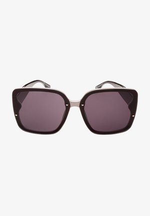 Gafas de sol con montura negra sobredimensionada y angular, lentes tintados en gris y acentos de metal en el puente y las patillas.