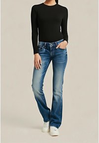 Czarna bluzka z długim rękawem w zestawieniu z jasnoniebieskimi rozszerzanymi jeansami, ozdobionymi efektami wyblaknięcia i dwoma przednimi kieszeniami, uzupełnione białymi sportowymi butami.