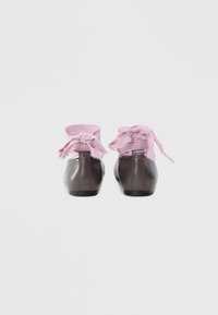 Pair of dark brown leather ballet flats with wide pink fabric ankle ribbons tied in bows, displayed against a white background.