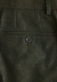 Dunkelgrüner, strukturierter Stoff mit einem subtilen Karomuster, ergänzt durch einen einzelnen Knopfdetail an einer Gesäßtasche, das einen funktionalen Akzent setzt.
