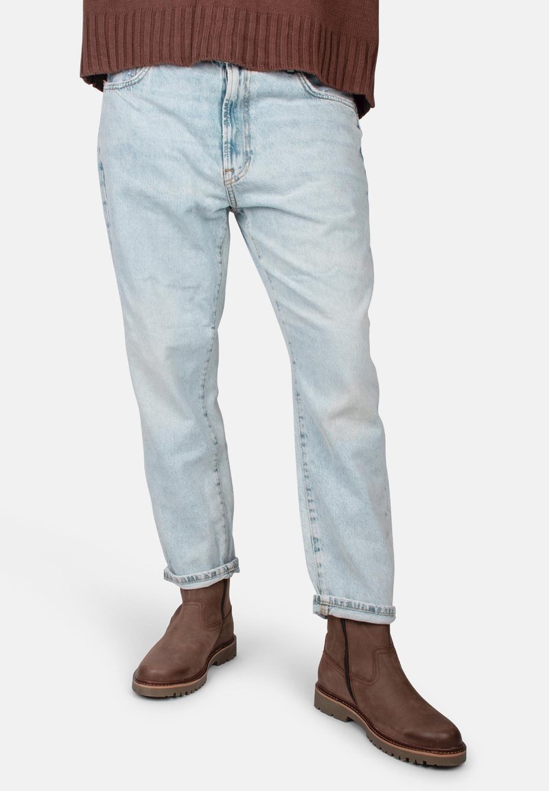 Jeans celeste chiaro a vestibilità comoda con texture sbiadita e orli risvoltati, abbinati a stivaletti marroni in pelle con suola in gomma.