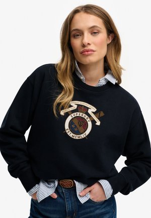 Marine sweatshirt met geborduurd logo en tekst, voorzien van een ronde hals en een ontspannen pasvorm. Draag over een lichtblauw gestreept shirt.