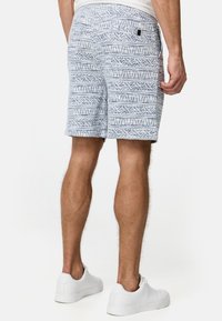 Pantalones cortos ligeros para hombre en color azul claro con un patrón geométrico, tejido elástico, bolsillos laterales y una etiqueta de logo en la parte trasera. Combinados con zapatillas blancas.