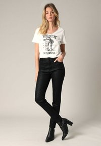 T-shirt blanc avec impression graphique noire, associé à un pantalon slim texturé noir et des bottines à talons noires. Design simple et ajusté.