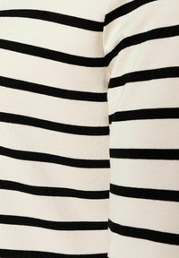 Schwarz-weiß gestreifter Stoff mit horizontalen Linien. Weiche Textur aus gestricktem Material. Sichtbare Nähte entlang der Kanten.