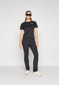 Black athletic shirt and pants made of moisture-wicking fabric. Pants feature zippered pockets and reflective accents. Model wears sunglasses.