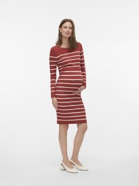 Piros csíkos kismama ruha hosszú ujjakkal, bordázott textúrával, testhezálló fazonnal és térdig érő hosszúsággal. Fehér pántos cipővel viselve.