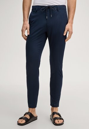 Pantaloni slim-fit blu navy con coulisse in vita indossati con sandali neri a doppio cinturino su una persona in piedi.
