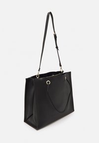 Bolso tote negro con una textura suave, forma acampanada, dos asas para el hombro, accesorios en dorado y diseño de apertura superior.