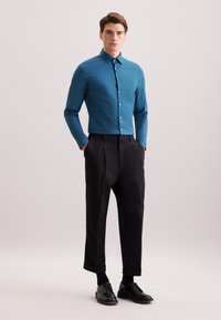 Teal shirt met aansluitende pasvorm en een gestructureerde kraag, knoopsluiting; gecombineerd met zwarte, geplooide broek en zwarte veterschoenen. Gladde stoftextuur.