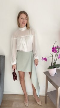 Blusa branca transparente com colarinho de babados, combinada com uma saia verde menta assimétrica. Acessórios incluem uma bolsa bordeaux e sapatos de salto nude.
