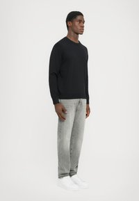 Pulover negru din tricot, cu guler rotund, ajustat pe corp. Asortat cu blugi drepti gri deschis și adidași albi. Design simplu și modern.