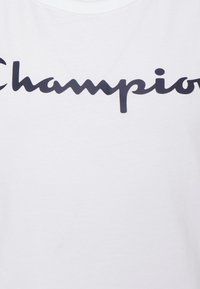 Bílý bavlněný tričko s výrazným černým logem "Champion". Látka je hladká s klasickým designem kulatého výstřihu.