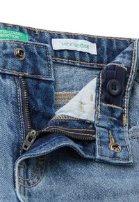 Jeans de mezclilla en un lavado azul claro con costuras amarillas en contraste, cremallera y cierre de botón. La etiqueta interior dice "MICK-LOOSE".