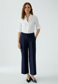 White button-up shirt with rolled sleeves, paired with navy wide-leg trousers featuring a textured waistband. Black pointed-toe shoes complete the look.