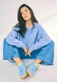 Felpa oversize azzurro chiaro, jeans denim a gamba larga e sneakers blu con dettagli gialli. Texture liscia in uno stile casual e rilassato.