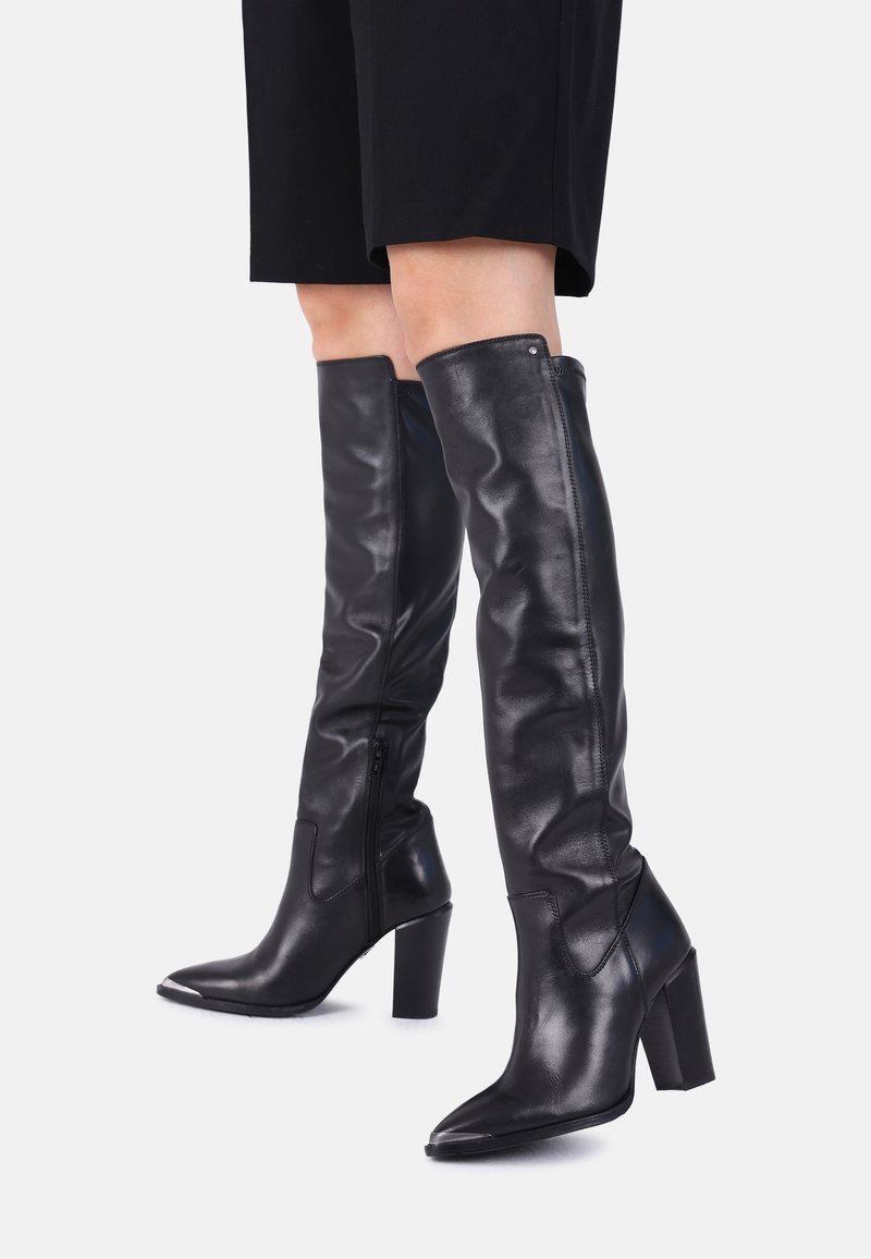 Botas negras de cuero que llegan por encima de la rodilla, con punta puntiaguda, tacón alto de bloque, cremallera lateral y textura lisa. Detalles sutiles de costura realzan el diseño.