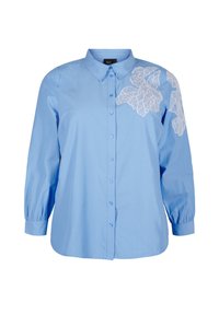 Camicia azzurro chiaro con maniche lunghe a palloncino, caratterizzata da ricami in pizzo bianco a forma di foglia sulla spalla destra e colletto classico.