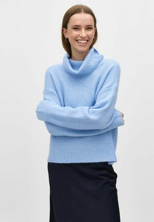 Cowl neck, light blue sweater in soft texture, relaxed fit with ribbed hem and cuffs, paired with a dark skirt.