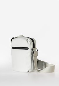 Borsa a tracolla sintetica bianca con tasca frontale con zip, cinturino regolabile e superficie liscia. Forma rettangolare compatta.