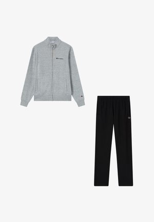 Grauer Sweatshirt mit Reißverschluss und Champion-Logo auf Brust und Ärmel, kombiniert mit schwarzen Hosen mit elastischem Bund und kleinem Champion-Logo am Oberschenkel.