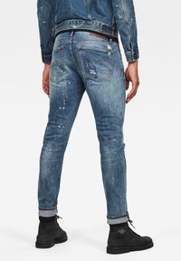 Bleka blå denimjeans med slim-fit design, slitna detaljer, färgfläckar och uppkavlade muddar. Bakfickor synliga.