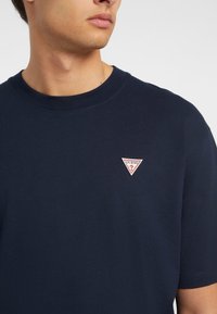 Marineblå bomulls t-skjorte med rund hals og korte ermer, med en rød og hvit trekantet logo på venstre bryst.
