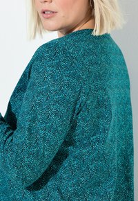 Tearfärgad mönstrad tröja med en texturerad yta, som har rund halsringning och långa ärmar. Designen innehåller små, oregelbundna former runtom.