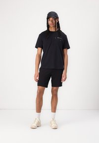Sort t-shirt med korte ærmer, sorte shorts, sort kasket, lyse sneakers. Simpelt design, glat tekstur, ingen mønstre eller synligt hardware.
