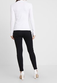 Top bianco a maniche lunghe abbinato a pantaloni neri aderenti, caratterizzati da una texture liscia e un design elegante. Sandali bianchi con tacco alto completano l'outfit.