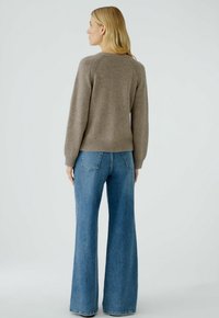 Brauner gestrickter Pullover mit geripptem Saum und langen Ärmeln, kombiniert mit hochtaillierten, weiten blauen Jeans. Glatte Textur und lässige Passform.