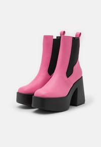 Botines de cuero rosa con paneles elásticos negros, suelas de plataforma gruesas en negro, textura suave y una lengüeta para facilitar el uso.