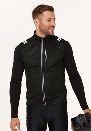 Schwarze Radfahren-Weste mit hohem Kragen, Frontreißverschluss und reflektierenden Akzenten. Glatte Textur, ärmelloses Design und sportliche Passform über schwarzen Hosen.