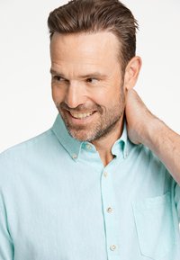 Jasnoniebieska koszula z guzikiem z fakturowanej tkaniny, z kieszenią na piersi i klasycznym kołnierzykiem. Wyraziste akcenty w postaci guzików wzbogacają design.